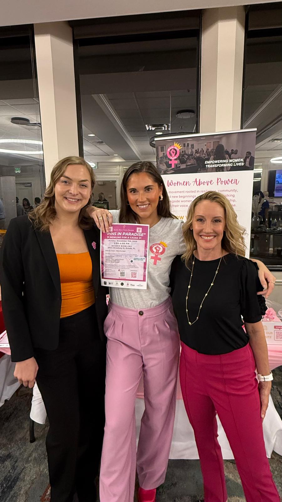 Three women posing together with a poster in an indoor setting